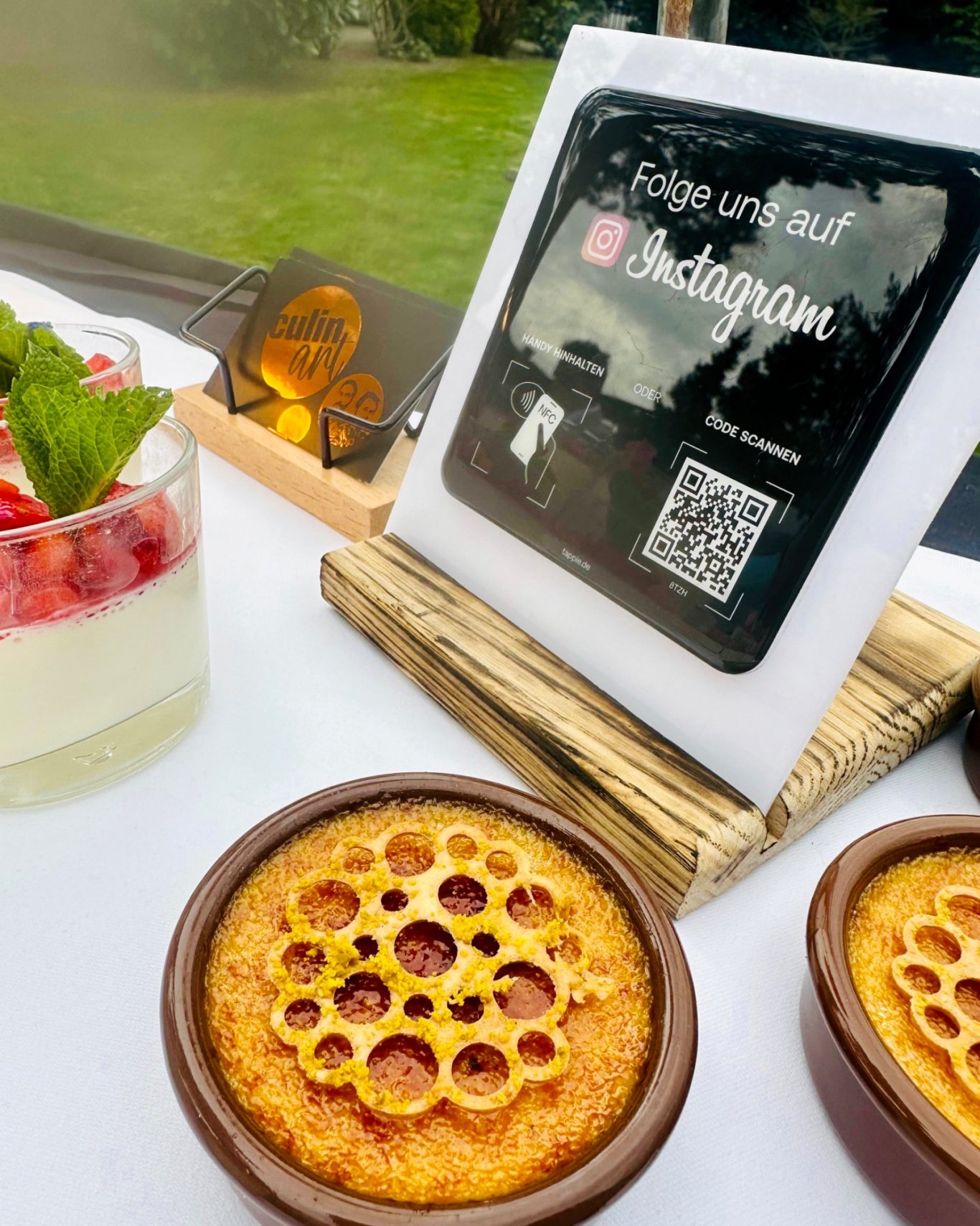 Crème brûlée in Tonschälchen und Erdbeer-Dessert im Glas neben dem Instagram-Aufsteller von CulinART