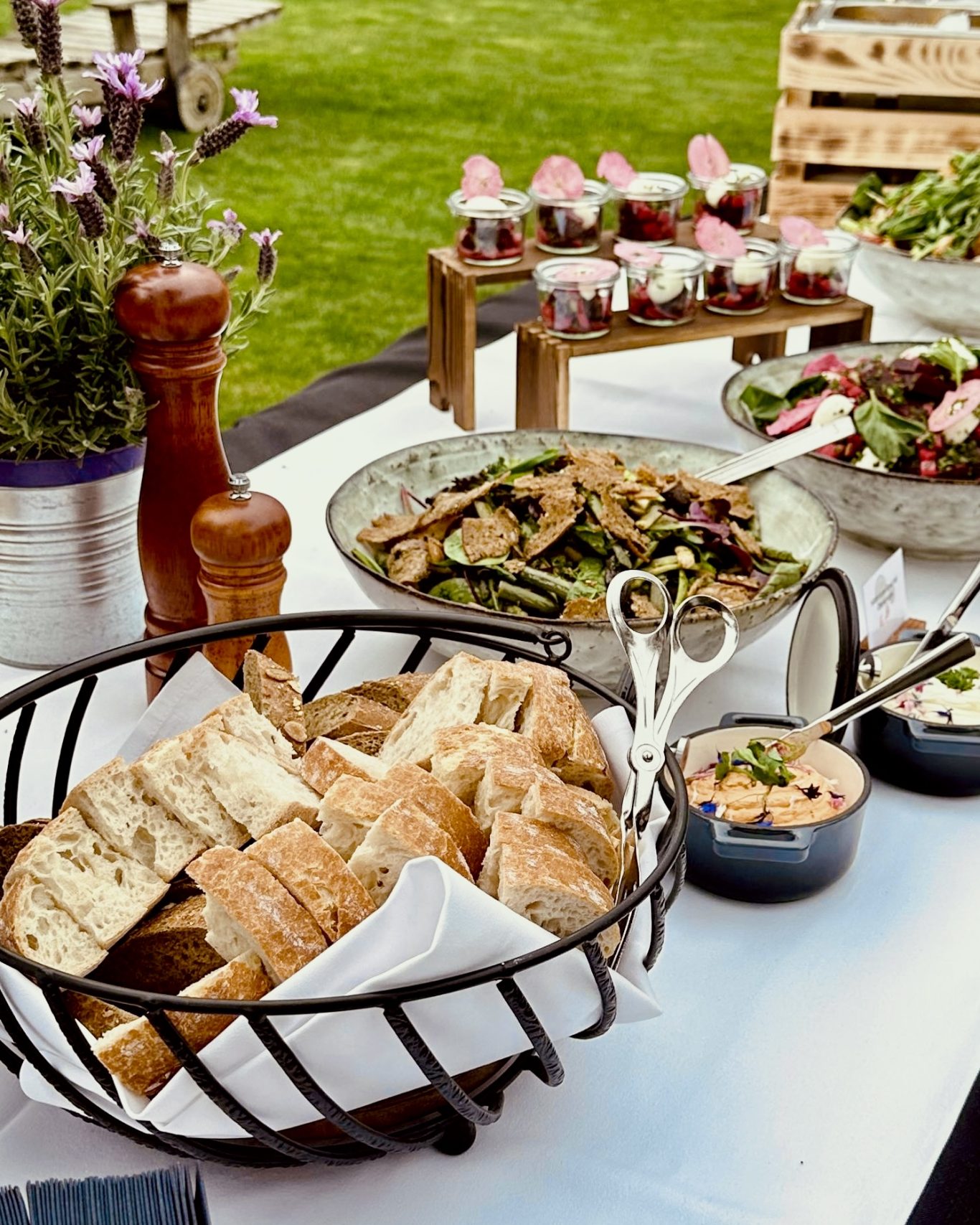 Brotkorb mit Baguette und Sauerteig, dahinter Salatschalen und Vorspeisen im Glas auf der Buffettafel